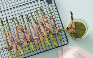 Hele grønne asparges svøbt i bacon, serveret med grøn pesto